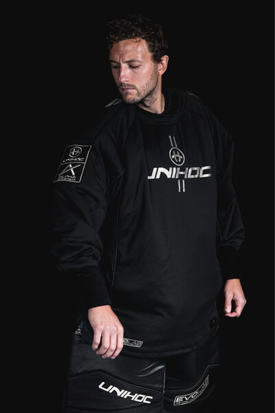 A man in a black Unihoc goalie uniform against a dark background.
